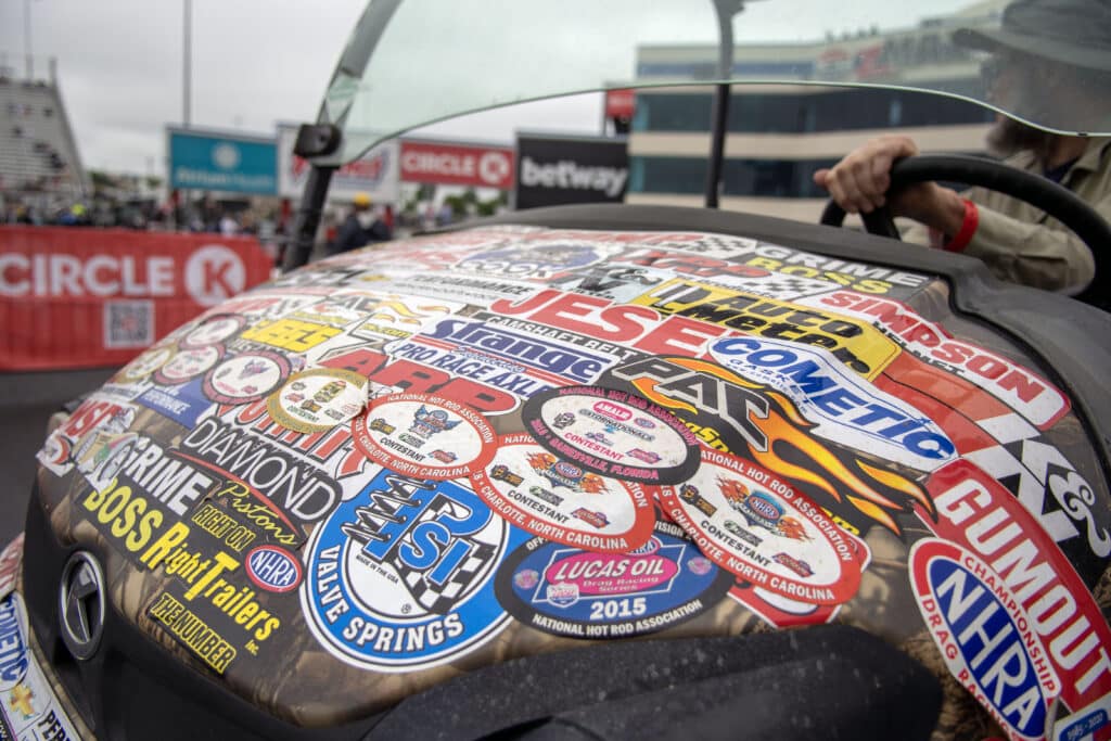 a golf car with lots of stickers on the hood at an nhra race