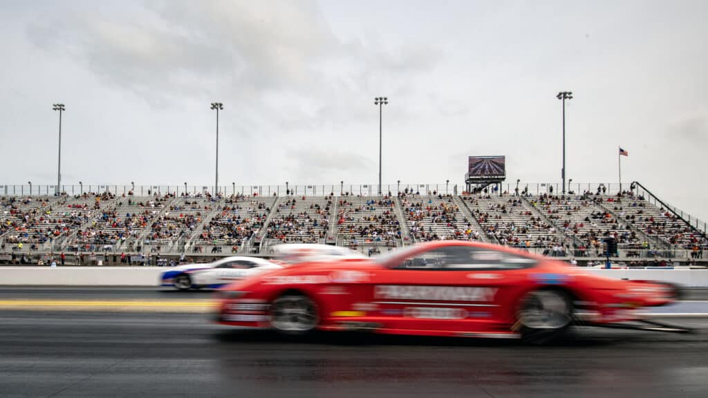 nhra pro stock cars racing with a red car blurred in the foreground