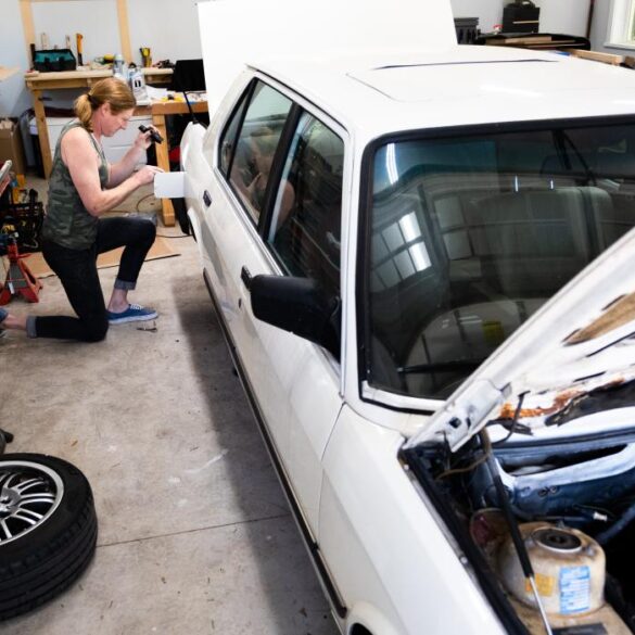 anna hursley works on her 1988 white bmw in the back of her garage